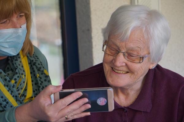 a lady wearing a face mask showing an elderly lady an image on a phone