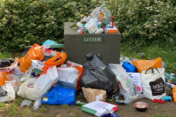 a full public rubbish bin surrounded by additional bags of rubbish