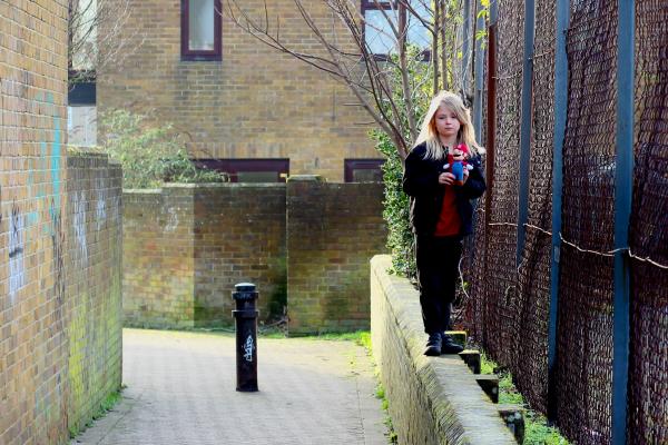 a young girl walking along a wall in a lane in a housing estate